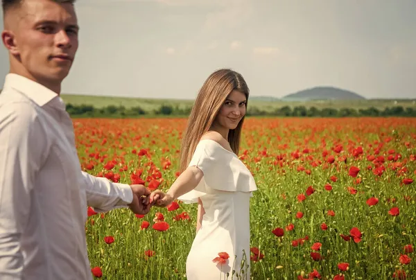 Feliz pareja enamorada caminando en el hermoso campo de flores de amapola en el día romántico, el amor — Foto de Stock