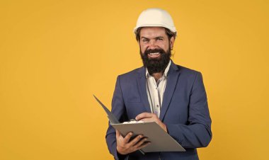 Proje üzerinde çalışıyorum. bina konsepti. Başlık takan mühendis ya da inşaatçı. Miğferli mutlu mimar notlar alıyor. Vahşi sakallı adam belgelerle inşaat alanında çalışıyor.