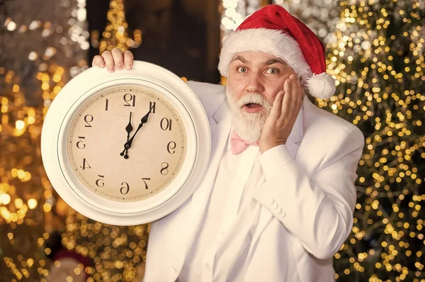 新年のカウントダウン。レトロな時計の男。ガーランド照明の背景。サンタの帽子の髭のビジネスマン。クリスマス・イブ。タキシード姿のサンタさん。サンタは時間を数える。真夜中のコンセプト — ストック写真