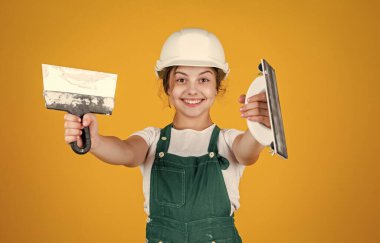 Sanırım sana yardım edebilirim. Kasklı çocuk inşaat alanında. Alet spatulası olan genç bir sıva ustası. Çocuk tamir işiyle uğraşıyor. Atölyede yenileme konsepti. Meşgul profesyonel marangoz malayla