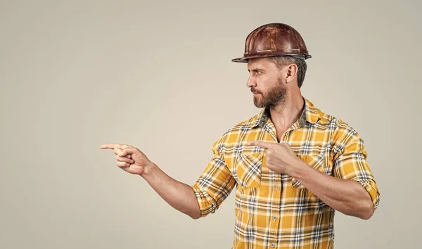 Bel homme réparateur dans la construction casque de sécurité et chemise à carreaux sur le chantier de construction pointant finegr, espace de copie, publicité — Photo