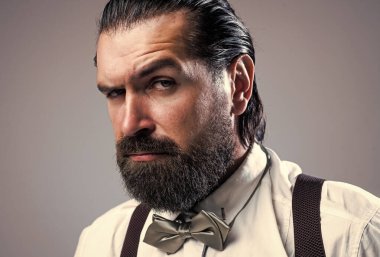 Bıyıklı beyaz sakallı adam pantolon askısı ve papyon takıyor, erkek modası.