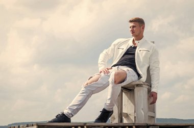 Rahatlamış seksi bakışlar. Seksi adam, bulutlu gökyüzüne otur. Yakışıklı adam açık havada rahat giyiniyor. Moda dolabı. Tatil zamanı. Eğlence etkinliği. Dolaşmak ve seyahat etmek. Bakım özgürlüğü