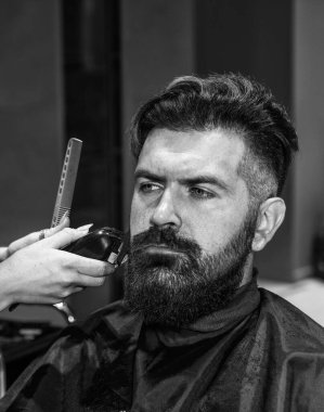 Berber dükkanına gelen olgun, beyaz bir adam bir kuaför, kendine bakan, erkeksi bir güzelliğin yardımıyla sakal ve saç getiriyor.