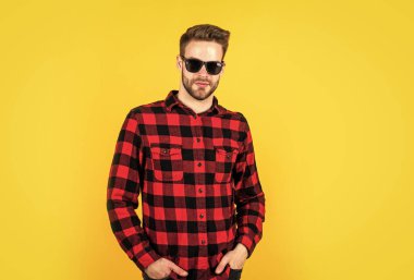 Havalı ve seksi. İyi bakımlı bir saç stili. Erkek güzellik ve moda. Sakallı adam için kareli gömlek. Tıraşsız, güneş gözlüklü yakışıklı adam. Kuaför konsepti. Genç ve kendinden emin