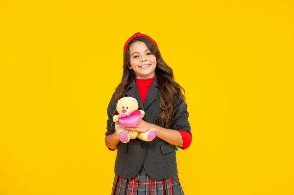 Усміхнена дівчина-підліток в уніформі тримає іграшку на жовтому фоні, назад до школи — стокове фото