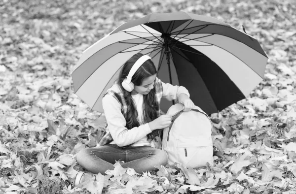 傘の下の秋の子供。本を読むことになります。幸せな子供時代。学校に戻って。バックパック付きヘッドセットの女の子は公園でリラックスします。森で秋をお楽しみください。音楽を聴け。オンラインコース教育 — ストック写真