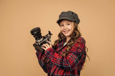 Kareli ceketli mutlu fotoğrafçı kız. İlkbahar çocuğu fotoğraf makinesi kullanıyor. Şapka takan çocuk. Eski teknoloji. çocukluk mutluluğu. Paris 'in retro görüntüsü. Fransız modası. Harika bir tarzı var.