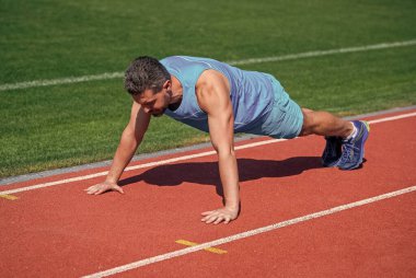 Güçlü kaslar. erkek gücü ve gücü. Tahtadaki sporcu. Sporcu şınav çeker. Çekirdek kaslarını çalıştırın. Stadyumda şınav çeken bir adam. Spor salonu açık havada. Kaslı atletizm antrenmanı