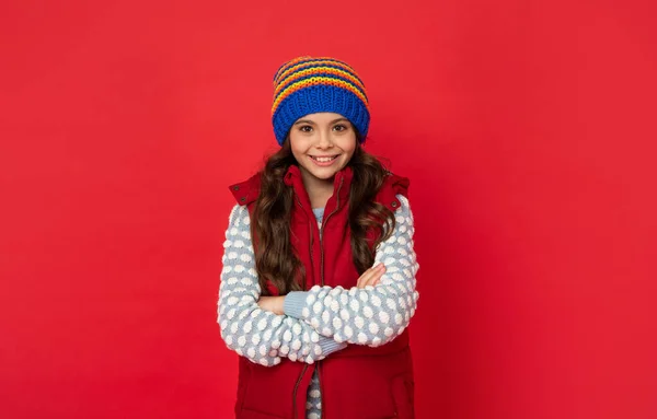 Bambino allegro in maglia cappello invernale e piumino mani incrociate su sfondo rosso, stagione fredda — Foto Stock