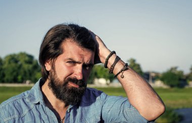 Harika bir tarzı var. Kendine güvenen ve yakışıklı bir adamın bahar portresi. Vahşi sakallı adam günlük gömlek ve güneş gözlüğü takıyor. Erkek yaz modası ve güzellik. Bıyıklı, vahşi, beyaz bir hippi.