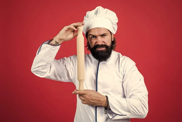 Confiante chef cara com barba e bigode no cozinheiro uniforme segurar rolo pino, utensílio de cozinha — Fotografia de Stock