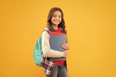 Mutlu okul çocuğu ders kitaplarını 1 Eylül 'de sarı arka planda tutuyor, okula geri dönüyor.