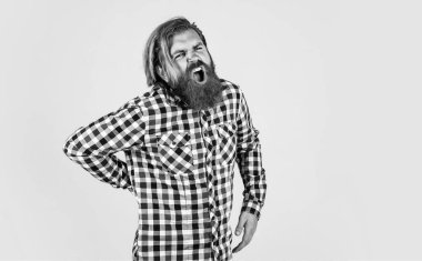 Vahşi sakallı adam kareli gömlek giyer sakalı ve bıyığı gür Sırtında ağrı hisseder, ilaç