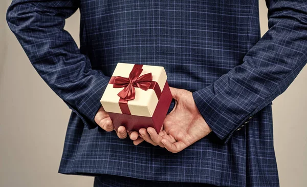 Caja de regalo atada con lazo de cinta roja sostenida en manos masculinas detrás de la espalda en traje de moda de estilo formal, día de boxeo —  Fotos de Stock