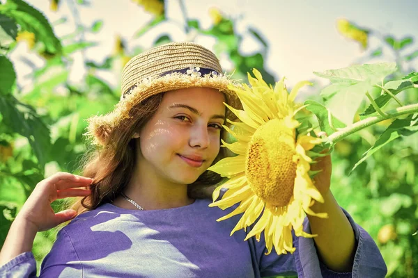 Az időjárás miatt. tini lány a napraforgó mezőn. a nyári vakáció fogalma. gazdag termés és mezőgazdaság. Boldog gyermekkort. A gyerek szalmakalapot visel. gyermek mező sárga virágok — Stock Fotó