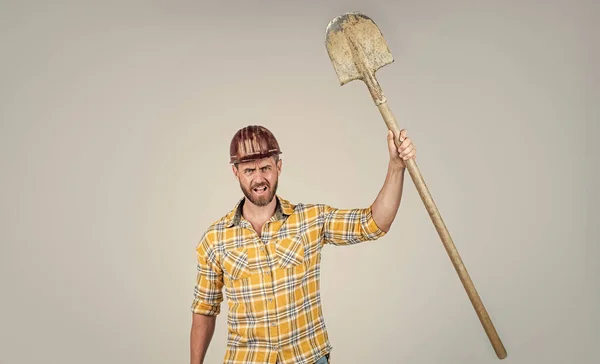 Красивый мужчина подрядчик в шлеме безопасности строительства и клетчатой рубашке на строительной площадке с лопатой, день труда — стоковое фото