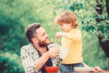 Yemek alışkanlıkları. Babası yla birlikte yiyecek doğa geçmişi yiyen küçük bir çocuk. Yaz kahvaltısı. Sağlıklı gıda kavramı. Baba oğul yemek yer ve eğlenir. Bebeği besliyor. Çocuklar için menü. Aile ev yapımı yemeğin tadını çıkarıyor