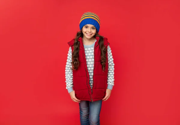 Szczęśliwy nastolatek dziewczyna w dzianiny czapka zimowa i dół kamizelka stojąca na czerwonym tle, zima — Zdjęcie stockowe