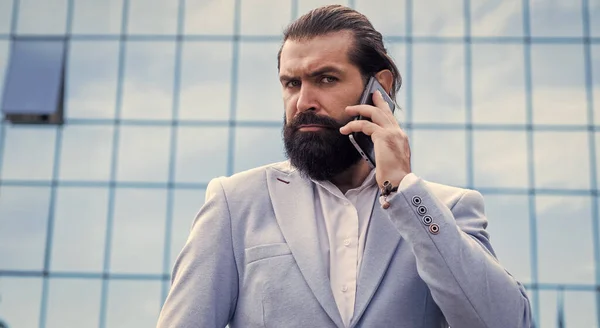 Красивый взрослый бородатый мужчина в костюме говорит по телефону на открытом воздухе, ловкий бизнес — стоковое фото