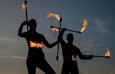 Meydan okumaya yükselin. Seksi çift yanan çubukları manipüle ediyor. Karanlık siluetler gökyüzünde ateş çubukları çeviriyor. Sopa çevirme. Yangın gösterisi. Açık hava festivali. Gece partisi. Ateş ve duman