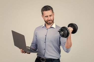 Çevrimiçi spor salonu verimliliği arttırıyor. Müdür, dizüstü bilgisayarın kıvrımlı dumbell 'ini tut. Dayanıklılık eğitimi. İş koçu. Fitness iş başında. Ağırlık kaldırma egzersizi. İş yeri spor salonu. Spor teknolojisi.