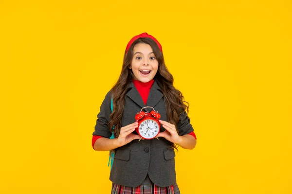 Niño sorprendido en uniforme escolar mantenga despertador sobre fondo amarillo, mañana — Foto de Stock