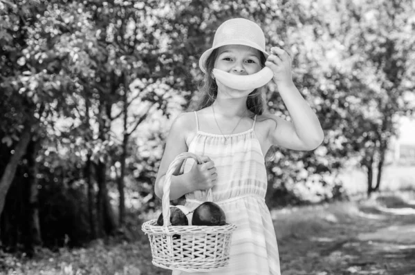 Бананова посмішка. Дівчина в саду тримає яблуко і кошик зібрані фрукти — стокове фото
