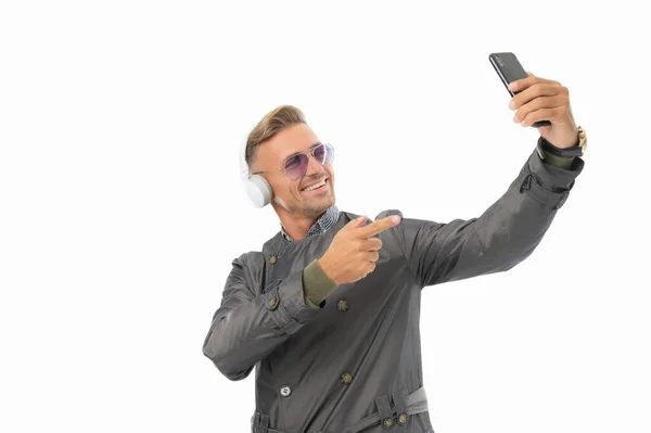 Szczęśliwy przystojny facet słuchać muzyki w słuchawkach wskazując palcem na telefon komórkowy, smartfon — Zdjęcie stockowe