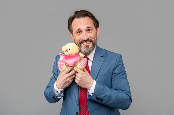 Om de afaceri senior fericit în costum țineți ursul de jucărie pe fundal gri, Ziua Îndrăgostiților — Fotografie, imagine de stoc