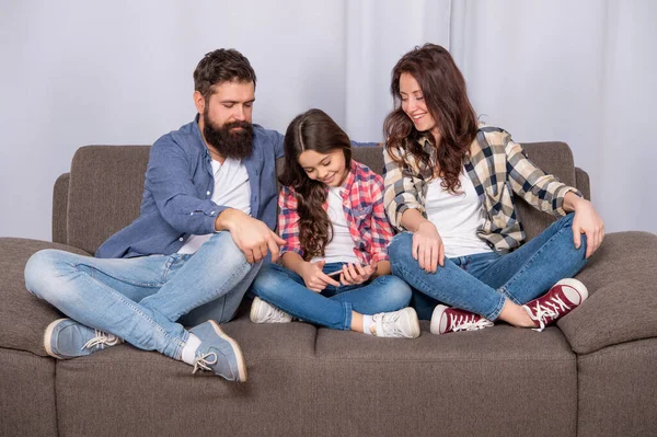 Criança feliz jogando jogos móveis no smartphone sentado ao lado de pai e mãe no sofá, família — Fotografia de Stock