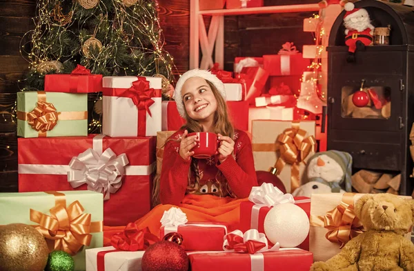 Gelukkige kindertijd concept. Kind gelukkig meisje vinden geschenken in de buurt van kerstboom. Vrolijk kerstfeest. Ontdek de schoonheid van de winter. Gezellig en hygge. Warme chocolademelk. Cadeauwinkel. Kid santa hoed kerst geschenkdozen — Stockfoto