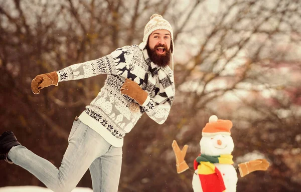 Veel plezier in de winter. Laat het sneeuwen. Kerstvakantie. Actieve levensstijl. Sneeuwspelen. Vrije tijd op frisse lucht. Man vrolijk baard hipster gebreide hoed en warme handschoenen spelen met sneeuwpop sneeuw buiten — Stockfoto