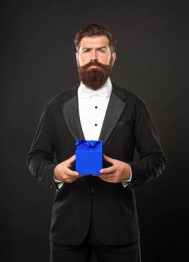 Smokinli olgun bir adam hediye kutusunu tutuyor.