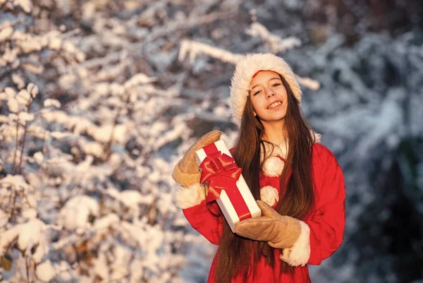Boldog karácsonyt! Boldog új évet! gyermek karácsonyi ajándékdobozzal. Töltsd a téli vakációt örömmel. Ajándék a Télapótól. Kislány vásárolni megy. Kislány télapó jelmezben a szabadban. havas téli természet — Stock Fotó