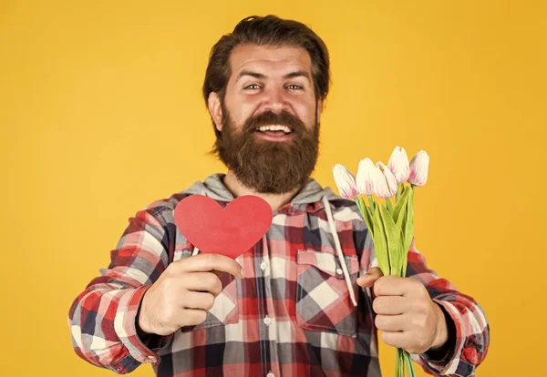 Buquê de primavera para ela. Pronto para um encontro romântico. presente para mulheres e mães dia. homem barbudo feliz segurar flores de tulipa e coração decorativo. Festa dos namorados. presente de aniversário feliz com amor — Fotografia de Stock