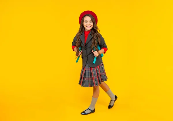 Gelukkig kind in school uniform met baret en rugzak lopen op gele achtergrond, schoolmeisje — Stockfoto