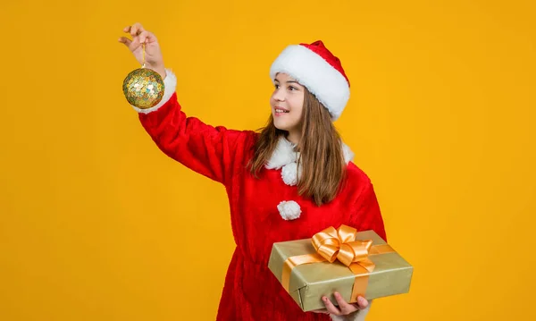 Dítě nosí červený klobouk držet dárkové krabice a stromové dekorace. dětský Santa pomocník v kostýmu. Večírek. připravte se na zimní dovolenou. Šťastný nový rok. Veselé Vánoce. veselý dospívající dívka slavit vánoční večírek — Stock fotografie