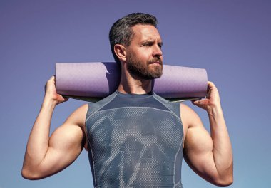 Gökyüzü arka planında yoga minderi olan pilates eğitmeni, spor