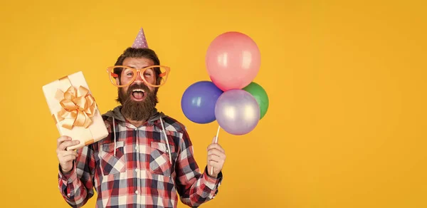 Parti balonları ve hediye kutusuyla damalı tişörtlü, olgun, yakışıklı bir adam. — Stok fotoğraf