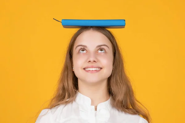 Cheerful child with school book on head on yellow background, knowleldge — Stockfoto