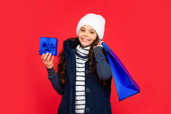 Cheerful kid in puffer jacket and hat. teen girl after shopping on red background. — Foto Stock