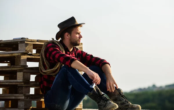 Romanticism of western culture. Farmer in hat sit relax. Farmer enjoy view from his farm. Peaceful mood. Watching sunset. Farmer cowboy handsome man relaxing after hard working day at ranch — Stock Photo, Image