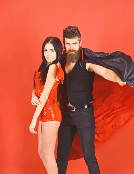 Attractive demon concept. Man and woman dressed like vampire, demon, red background. Couple in love, perfect match. Couple on strict face play role game. Vampire in cloak and sexy devil girl cuddlin — ストック写真