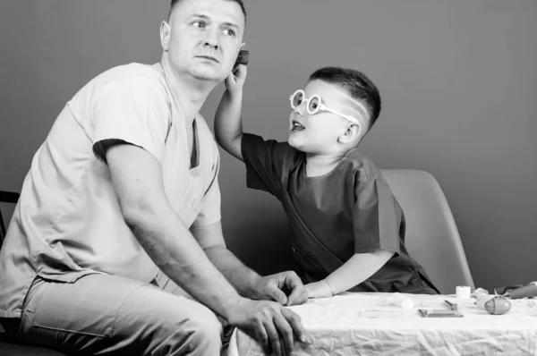 Un niño pequeño con papá en el hospital. niño feliz con padre con estetoscopio. médico de familia. medicina y salud. padre e hijo en uniforme médico. Un niño pequeño juega con su padre. doctor niño pequeño — Foto de Stock