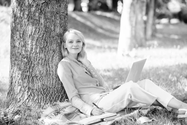 妇女与笔记本电脑工作户外靠在树干上。女孩在公园里用笔记本电脑工作坐在草地上。教育技术和互联网概念。自然环境办公室。户外工作优惠 — 图库照片