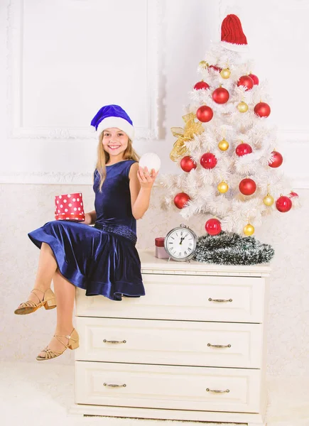 Παιδί κορίτσι κάθονται κοντά στο χριστουγεννιάτικο δέντρο κρατήστε κουτί δώρου. Μικρό κορίτσι santa καπέλο ενθουσιασμένος για δώρο Χριστουγέννων ή του παρόντος. Παιδί Γιορτάστε τα Χριστούγεννα στο σπίτι. Χρόνο για να ανοίξει τα δώρα Χριστουγέννων. Ευτυχισμένο το νέο έτος έννοια — Φωτογραφία Αρχείου