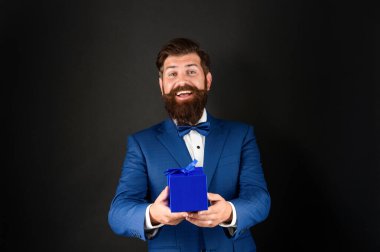 Smokinli mutlu adam siyah arka planda papyon takıyor ve erkekler günü için bir kutu hazırlıyor.