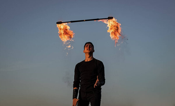 Male fire performer manipulate with flaming baton on blue sky outdoors, man
