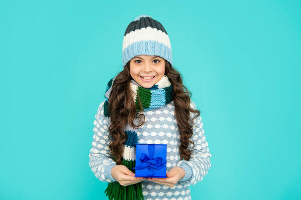 happy child in knitwear hold box. kid with present. teen girl on blue background. winter holidays